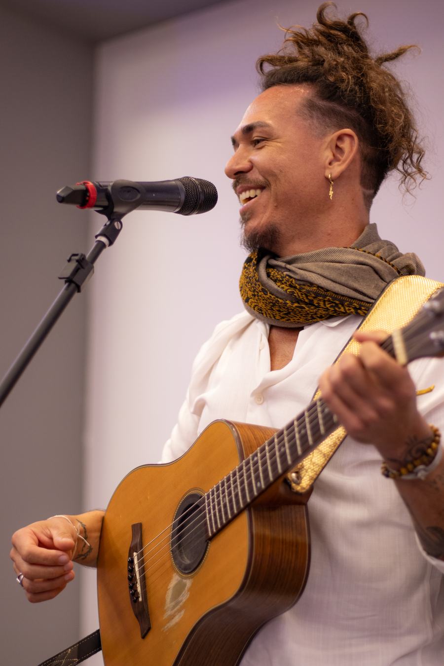 Diôgo Mar sorrindo, com o violão, ao microfone